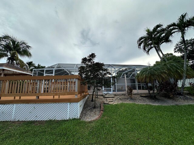 view of pool featuring a wooden deck, a yard, and glass enclosure