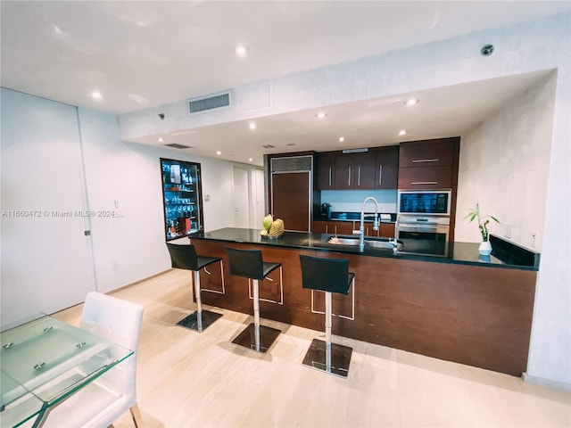 kitchen with light wood-type flooring, double oven, sink, and dark brown cabinetry