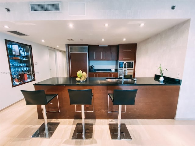 kitchen with built in microwave, a breakfast bar area, dark brown cabinets, and sink