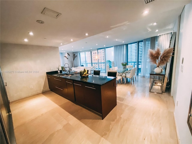 kitchen with sink, a wall of windows, dark brown cabinets, and a kitchen island with sink