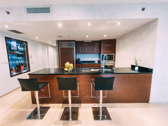 kitchen with built in appliances, a breakfast bar area, dark brown cabinetry, and sink