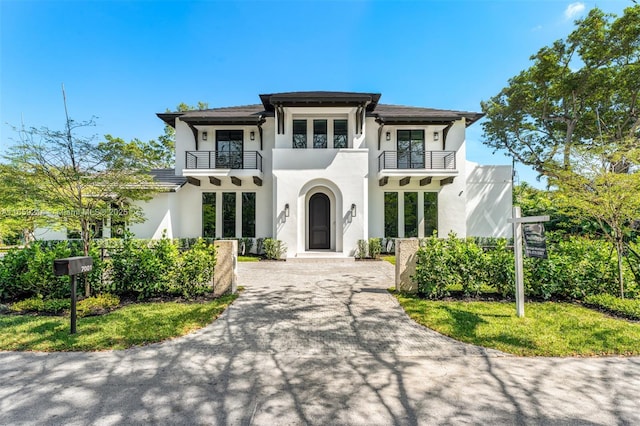 view of front facade featuring french doors, driveway, a balcony, and stucco siding