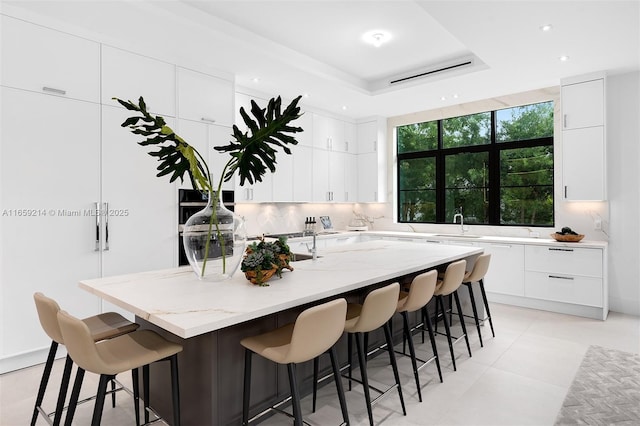 7001 SW 71st Ave, Miami, FL 33143 - kitchen with modern cabinets, a breakfast bar area, light stone countertops, an island with sink, and recessed lighting