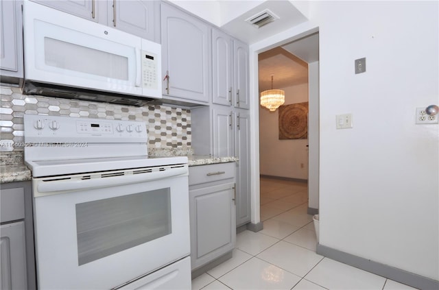 kitchen with light tile patterned floors, backsplash, an inviting chandelier, light stone counters, and white appliances