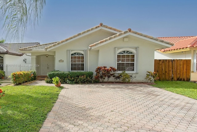 mediterranean / spanish home with a tile roof, stucco siding, and fence