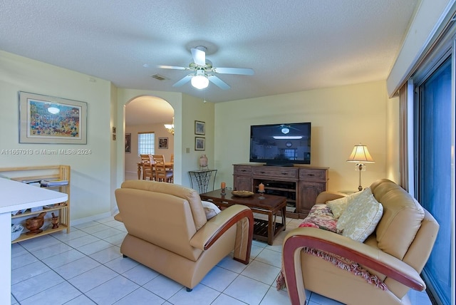 living area featuring light tile patterned floors, a textured ceiling, arched walkways, visible vents, and a ceiling fan