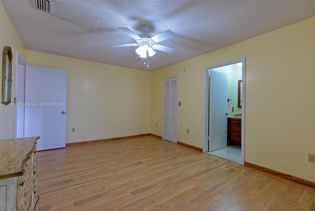 unfurnished bedroom with a textured ceiling, a closet, ensuite bath, ceiling fan, and light wood-type flooring