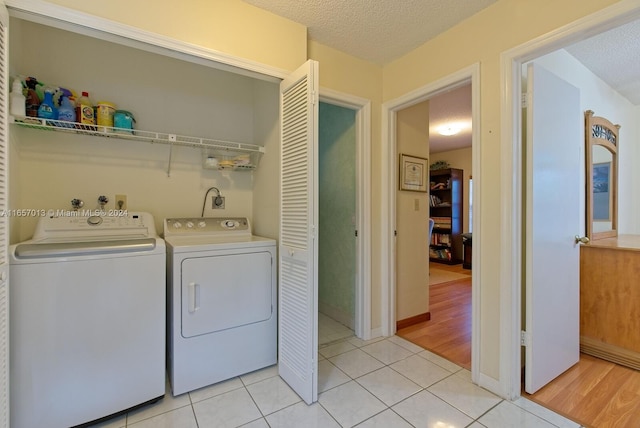 washroom with light tile patterned flooring, a textured ceiling, laundry area, baseboards, and washer and dryer