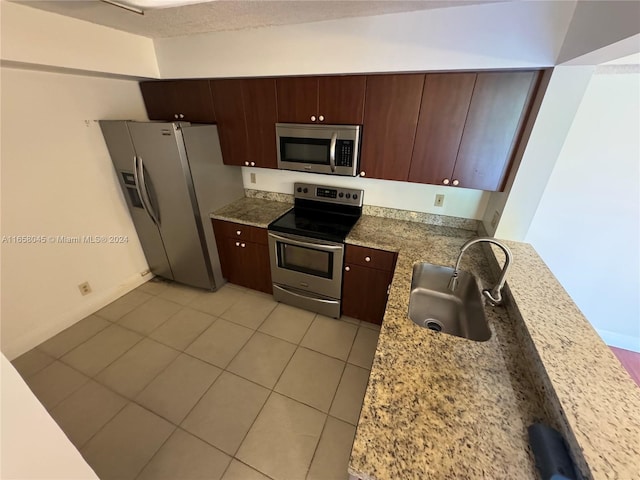 kitchen with appliances with stainless steel finishes, light stone countertops, light tile patterned floors, dark brown cabinets, and sink