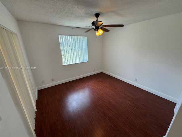 spare room with a textured ceiling, dark wood-type flooring, a ceiling fan, and baseboards