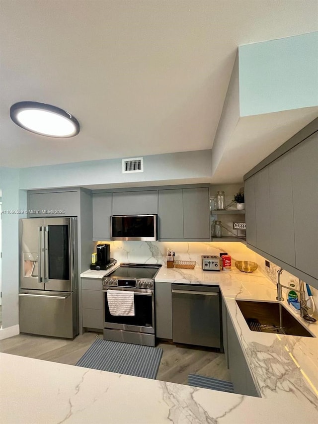 kitchen featuring a sink, appliances with stainless steel finishes, gray cabinets, and visible vents