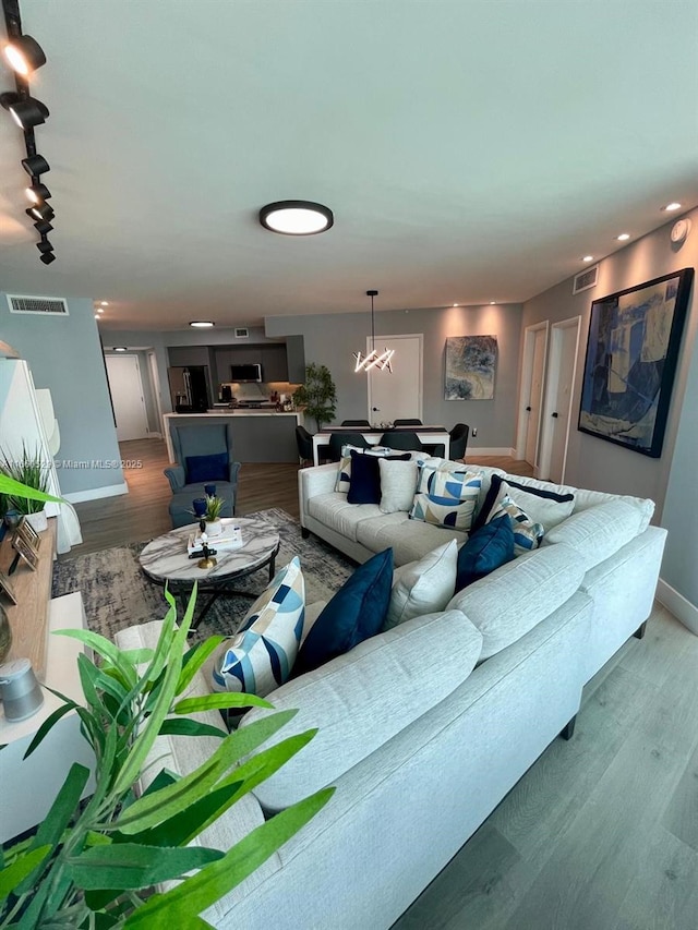 living room with rail lighting, wood finished floors, visible vents, and baseboards