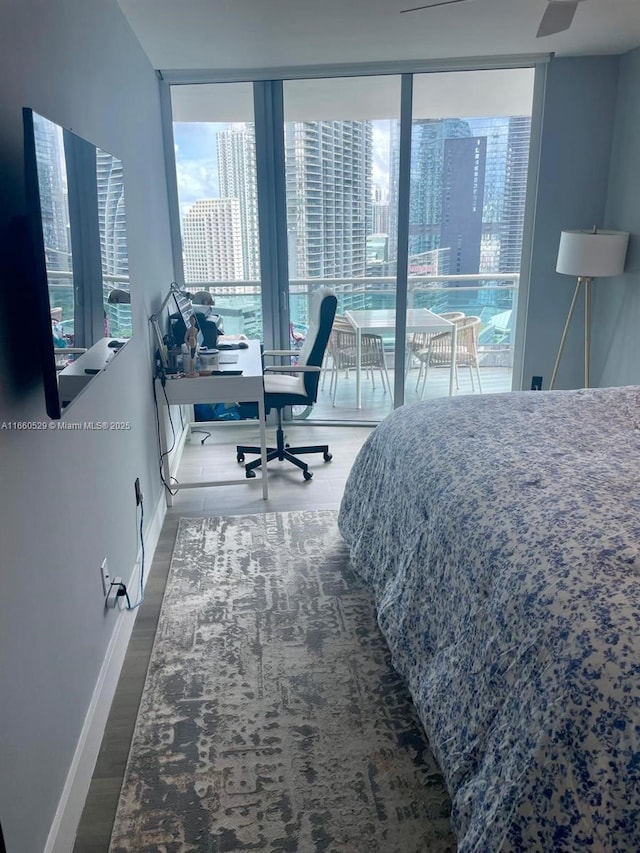 bedroom with a view of city, floor to ceiling windows, wood finished floors, and baseboards