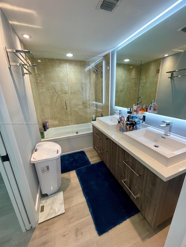 bathroom with wood finished floors, shower / bath combination with glass door, a sink, and visible vents