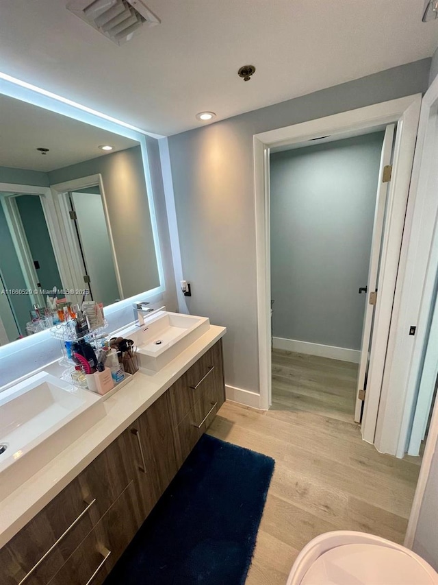 bathroom with a sink, wood finished floors, visible vents, baseboards, and double vanity