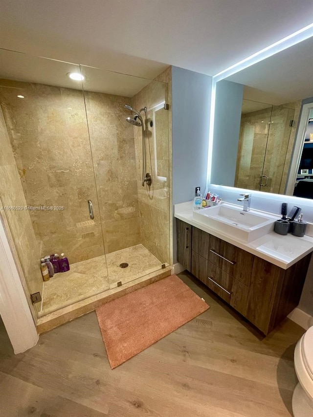 bathroom with toilet, a shower stall, wood finished floors, and vanity