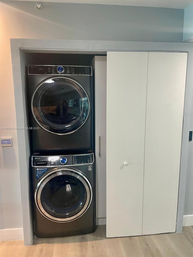 clothes washing area featuring stacked washer and clothes dryer, baseboards, and wood finished floors