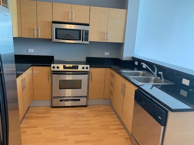 kitchen featuring dark stone counters, light hardwood / wood-style floors, kitchen peninsula, appliances with stainless steel finishes, and light brown cabinetry