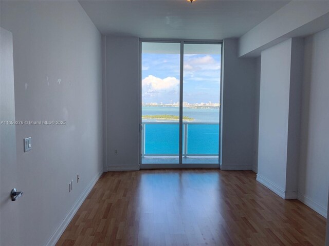 empty room featuring a wall of windows, wood-type flooring, and a water view