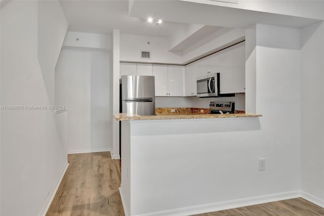 kitchen with light wood-type flooring, kitchen peninsula, white cabinetry, and stainless steel appliances