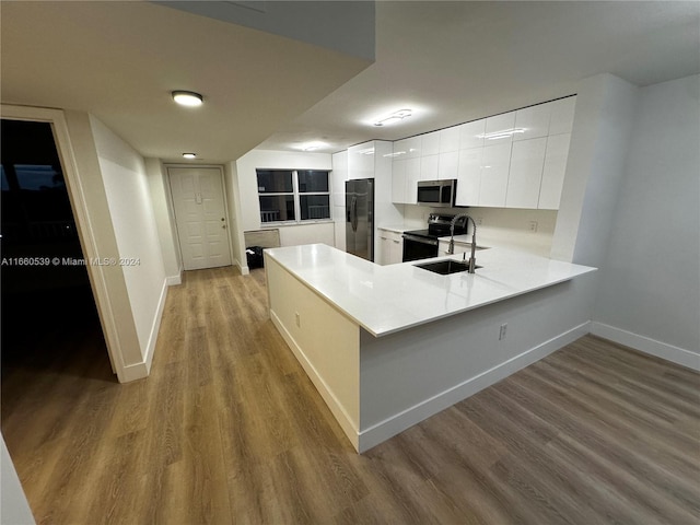 kitchen featuring kitchen peninsula, stainless steel appliances, sink, light hardwood / wood-style flooring, and white cabinetry