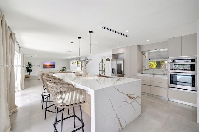 kitchen featuring light stone countertops, pendant lighting, appliances with stainless steel finishes, a kitchen bar, and a large island with sink