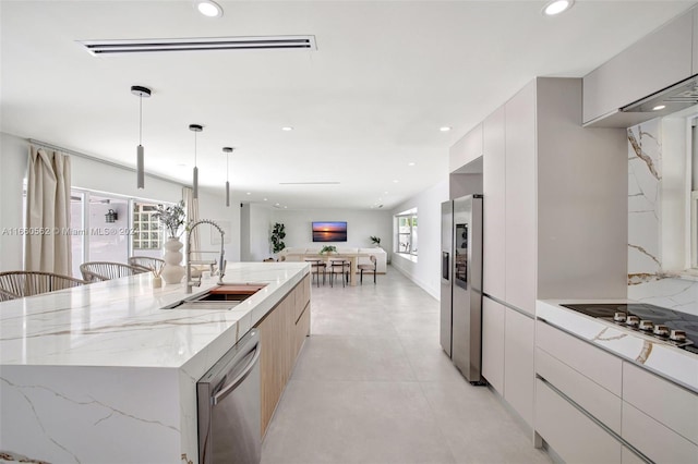 kitchen featuring a center island with sink, appliances with stainless steel finishes, hanging light fixtures, sink, and white cabinetry