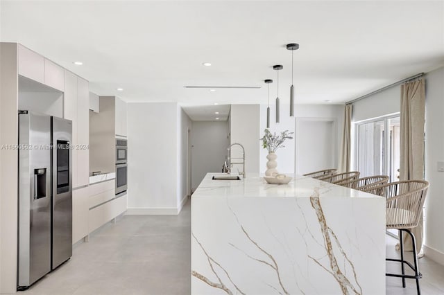 kitchen with white cabinets, decorative light fixtures, appliances with stainless steel finishes, light stone counters, and sink