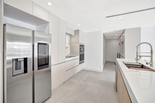 kitchen with appliances with stainless steel finishes, light stone countertops, sink, and white cabinets