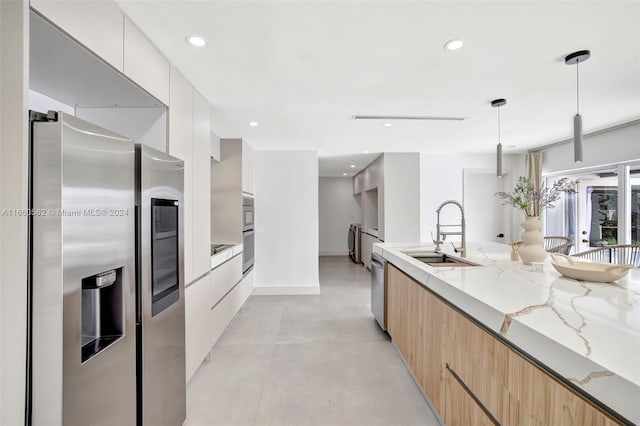 kitchen with white cabinetry, decorative light fixtures, light stone counters, sink, and appliances with stainless steel finishes