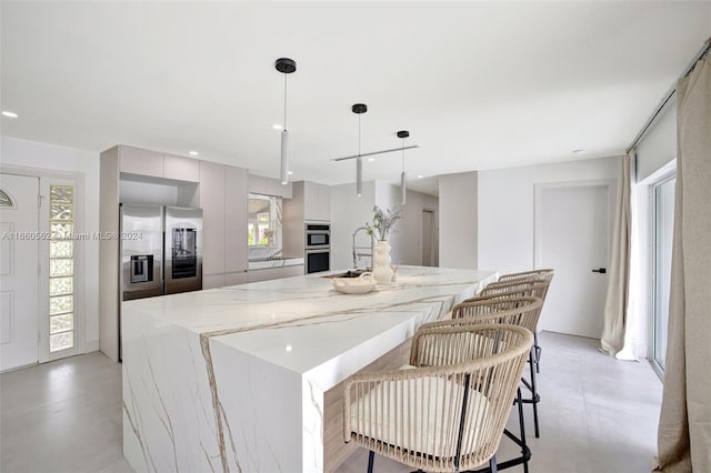 kitchen featuring gray cabinetry, decorative light fixtures, light stone countertops, stainless steel appliances, and a spacious island