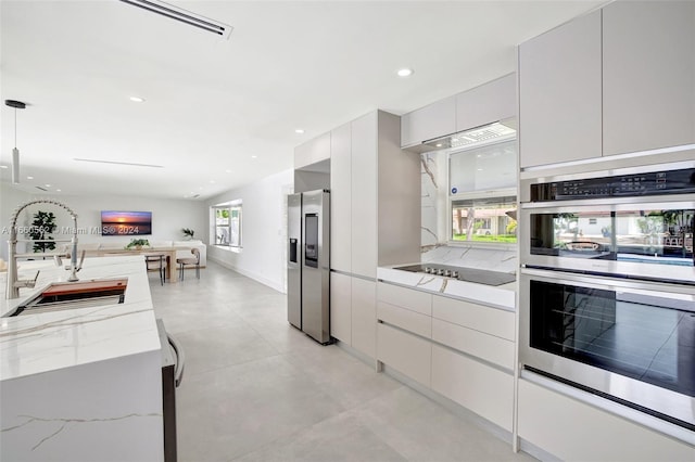 kitchen with appliances with stainless steel finishes, a healthy amount of sunlight, light stone counters, and decorative light fixtures