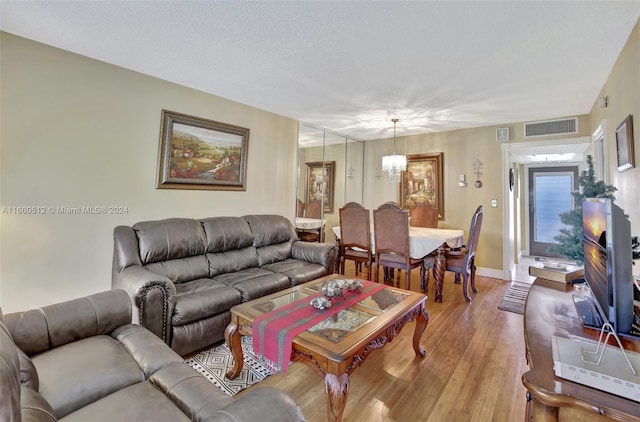 living room with an inviting chandelier, a textured ceiling, and light hardwood / wood-style flooring