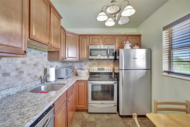 kitchen featuring an inviting chandelier, light stone countertops, backsplash, stainless steel appliances, and sink