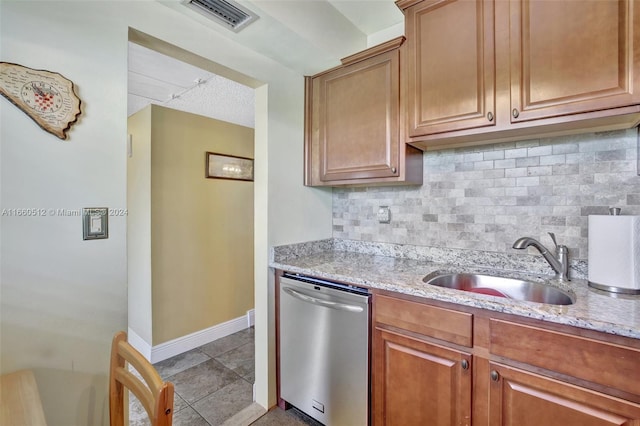 kitchen with light tile patterned floors, dishwasher, sink, light stone countertops, and decorative backsplash