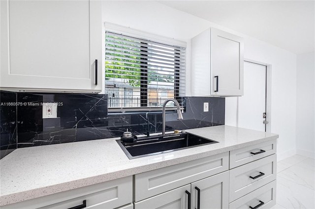 kitchen featuring tasteful backsplash, white cabinetry, light stone countertops, and sink