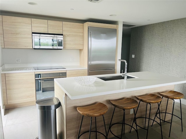 kitchen with light brown cabinets, sink, a center island with sink, appliances with stainless steel finishes, and tile patterned floors