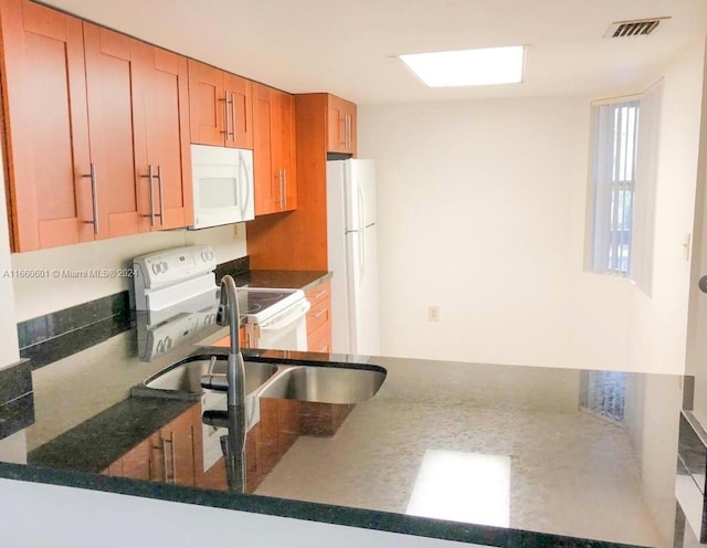 kitchen featuring white appliances, dark stone countertops, and sink