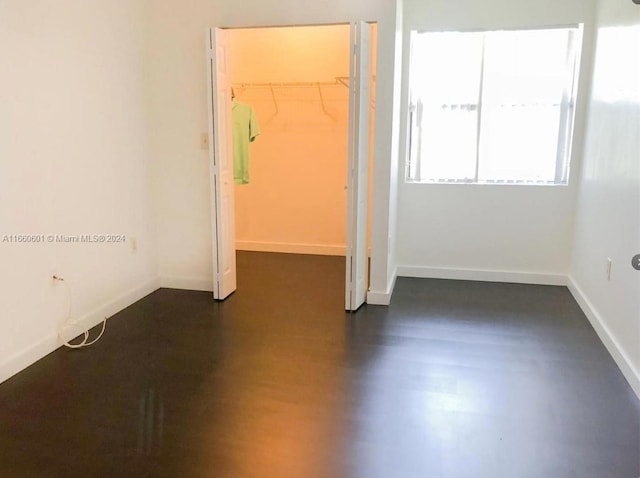 unfurnished bedroom featuring a spacious closet, dark wood-type flooring, and a closet