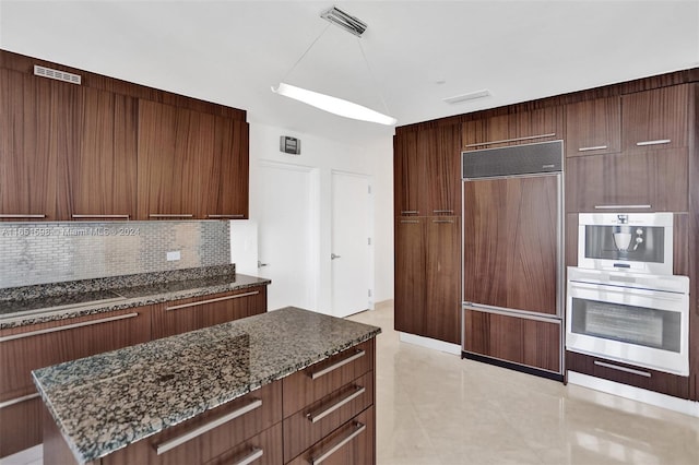 kitchen featuring paneled refrigerator, double oven, tasteful backsplash, and dark stone countertops