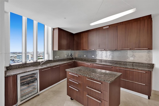 kitchen featuring sink, a kitchen island, beverage cooler, backsplash, and dark stone countertops