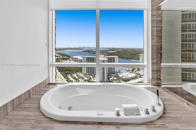 bathroom featuring a relaxing tiled tub, a water view, and a healthy amount of sunlight