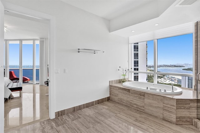 bathroom featuring a healthy amount of sunlight, a water view, and tiled tub