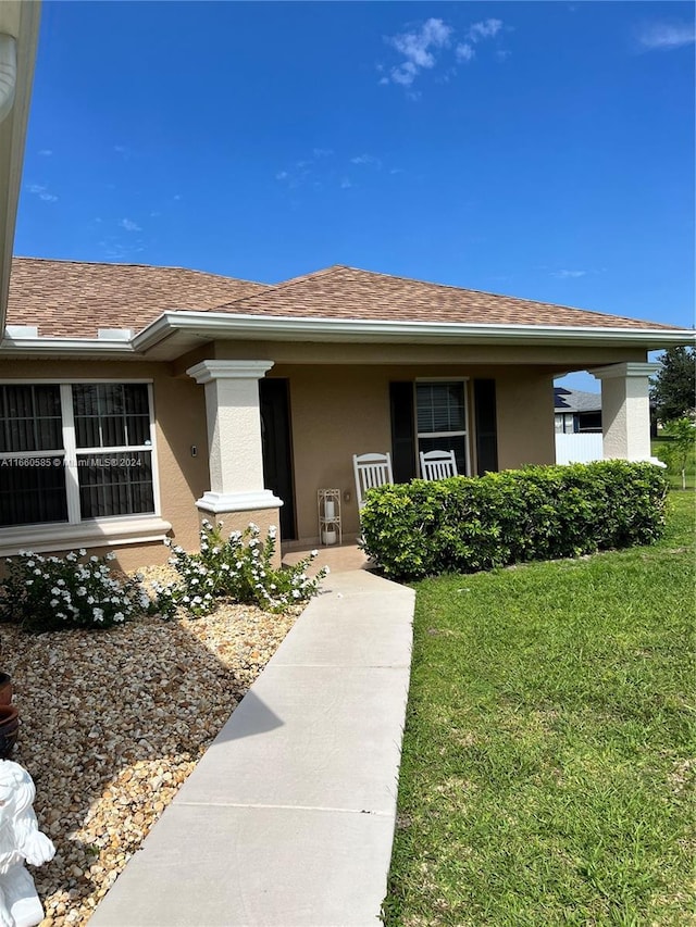 22 NW 17th Pl, Cape Coral, FL 33993 - doorway to property featuring a porch, stucco siding, roof with shingles, and a lawn