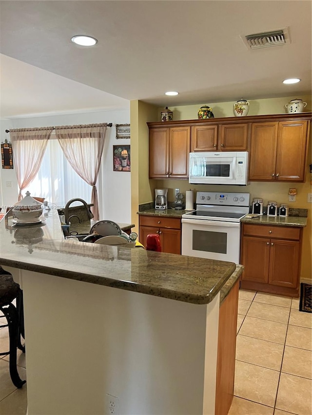 kitchen with white appliances, light tile patterned flooring, dark stone countertops, and a breakfast bar