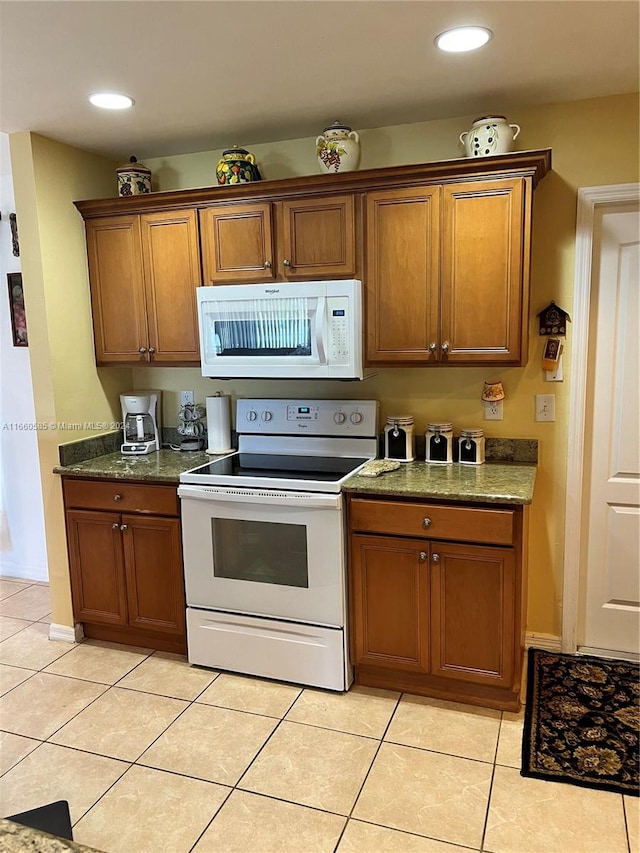 kitchen with white appliances, dark stone countertops, and light tile patterned floors