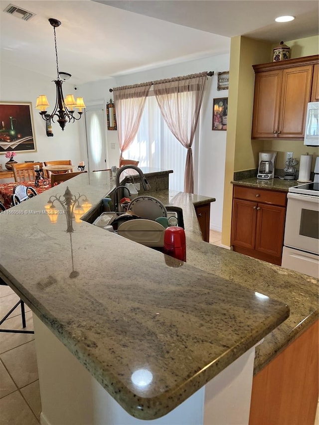 kitchen with white appliances, light stone countertops, pendant lighting, a kitchen bar, and an inviting chandelier