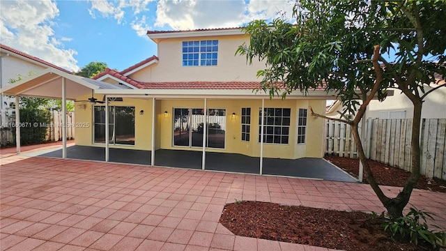 rear view of property with stucco siding, a tile roof, a patio, and fence