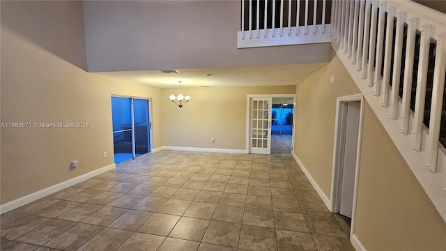 empty room featuring a textured ceiling, an inviting chandelier, a towering ceiling, and light tile patterned floors