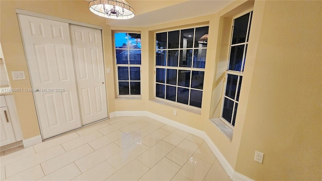 interior space featuring tile patterned flooring, a notable chandelier, and baseboards